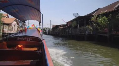 Düşük Açı: Longtail tekne güneşli bir günde kirli nehir üzerinde bir kanal üzerinden hızları. Bangkok Chao Phraya nehrinin diğer tarafında düzgün beton evler ile tezat bir tarafta Yoksul ahşap evler.