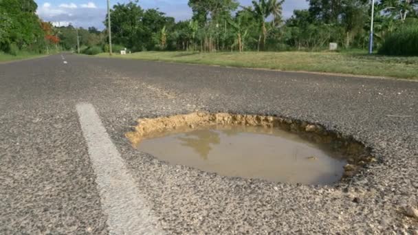 炎热的热带阳光照耀在穿过雨林的腐烂道路中间充满脏水的大坑坑上 雨后柏油路上的空洞满是浑浊的水 — 图库视频影像