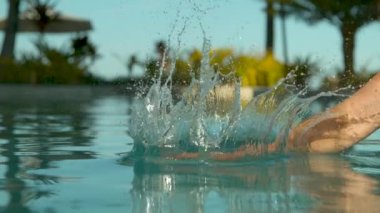 Slow Motion, Close Up: Lüks tatil havuzunda duran beyaz kadın durgun su yüzeyine çarpar. Genç gezgin Fiji harika bir tatil beldesinde uzanırken her yerde su sıçramaları.