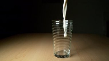 süper yavaş hareket: Lezzetli soğuk süt ahşap masa üzerinde boş bardağa dökülür. Beyaz sıvı akıyor ve boş camın etrafına sıçrıyor. Kahvaltıda cama dökülen lezzetli organik keçi sütü.