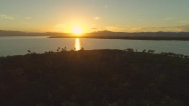 An, Lens Flare: Renkli yanık turuncu gün batımı huzurlu cennet adada aşağı parlar. Pitoresk akşam ışığı palmiye ağaçlarıile kaplı Fiji adasına yaklaşan sakin okyanus dalgalarını aydınlatır.