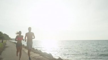 Portre, Lens Flare: Neşeli genç çift güneşli sahil caddesi ve yüksek beşli aşağı çalışır. Atletik kadın ve adam başarıyla okyanus yolu boyunca koşu kutlamak. Sportif Kafkas koşucuları koşuyonu bitirdi.