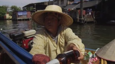 Bangkok, Tayland - Mart 2017, Close Up: Hasır şapka takan kadın, küçük teknesinden içecekler sunuyor. Yerel Tay kadın ahşap tekne taksi insanlara yön veren teknesinde oturan.