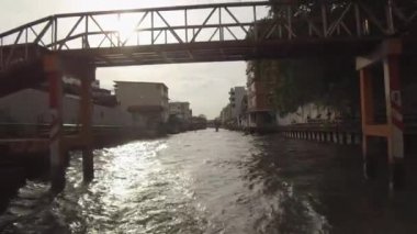 Lens Flare: Gün batımında kirli nehir kanalı geçerken eski köprüden uzağa sürükleniyor. Motosikletli tanınmayan adam güzel gün batımında nehir üzerindeki köprüyü geçerken kamera yavaşça uzaklaşıyor.