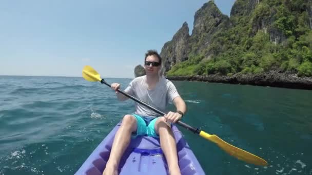 クローズアップ肖像画 絵のように美しいピピ諸島で彼のカヤックをパドリング楽しんでいる若い男性 白人男性は タイでカヤックしながら 見事な石灰岩カルスト島とターコイズブルーの海水を見ます — ストック動画