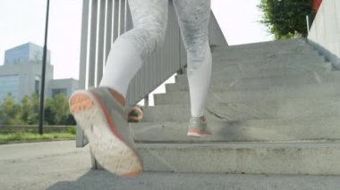 Yavaş Hareket, Düşük Açı, Lens Parlaması: Fit genç kadın beyaz sıkıştırma güneşli şehirde merdivenlerden yukarı çalışır. Şehir içinde güneşli bir sabah tanınamayan atletik kadın eğitim. Aktif uyum yaşam tarzı