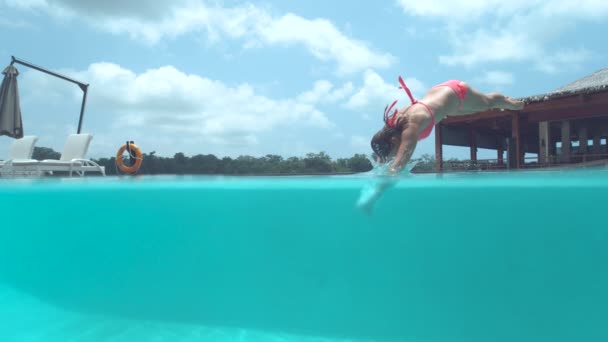 スローモーション ハーフ水中 遊び心のある若い女性旅行者は 空のプールに頭を最初にジャンプします 熱帯の島でリラックスした夏休みの白人女性は息をのむようなターコイズブルーの水に飛び込みます — ストック動画