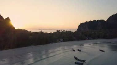 Hava Lens Flare Cennet Adası'nda kumlu plaj yakınında uçan insanlar pastoral gün doğumunda yürüyüşler alarak düşük gelgit. Demirli teknelerin doğal manzarasıile sakin sahil ve tatil evlerinin serin görünümü