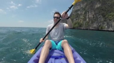 Close Up: Phi Phi Adaları etrafında kayak gezi neşeli erkek turist vicoriously başının üzerinde onun kürek kaldırır. Pitoresk egzotik Tay adaları etrafında eğlenceli kürek kayak sahip genç adam.