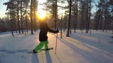 Close Up: Lapland ormanlarında kar ayakkabıları ile derin kar battaniye ile yürüyen genç kadın. Kış gün batımında taze toz karda kar ayakkabısı alan kız. İnsanlar gün doğumunda eğlenceli karlı kış egzersiz