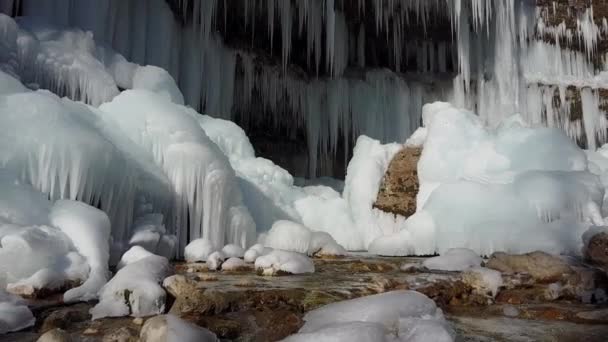 空中冬の川カスケードは白い輝くつららに凍った 冬の日に岩山の崖からぶら下がる見事な霜のつらら 早春の太陽が凍った滝の水滴を溶かす — ストック動画