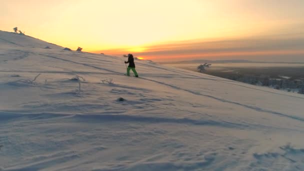 空中活跃妇女穿着冬衣雪鞋在雪山山坡上日出 年轻女子雪鞋徒步旅行在冬季日落 旅行者雪鞋探索雪拉普兰山脉在阳光明媚的早晨 — 图库视频影像