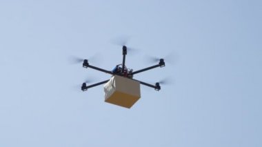 Yakın Uav insansız hava aracı teslimatı. Multicopter mavi gökyüzü üzerinde büyük kahverengi paket uçan. Drone evinize posta paketi teslim. Helikopter drone ile fütüristik sevkiyat. Multirotor lojistik ve taşımacılık