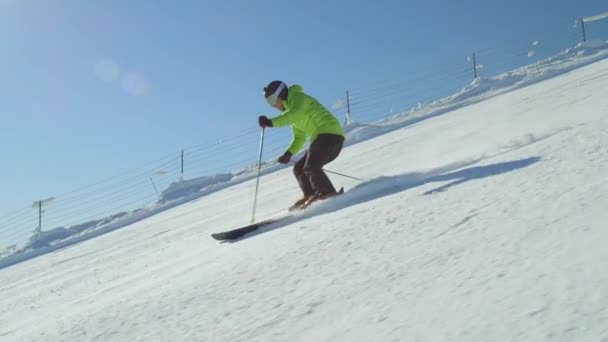 スローモーションの追跡 朝の太陽が谷の上に輝いている間 雪の多い冬の日に日当たりの良い山のスキーリゾートで斜面をスキーヘルメットを着用するプロスキーヤー アルプスヨーロッパに位置するスキーリゾート — ストック動画