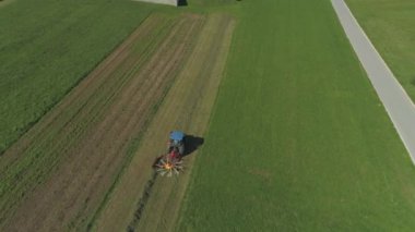 Havadan Yakın Madap Çim tarlasında çalışan mavi traktörün üzerinde uçmak, sonbaharın sonlarında kuru saman ları çevirmek. Çiftçi güneşli sonbaharda çayır tarım arazisi üzerinde çalışıyor. Tarım makineleri çalışma, kuru ot tornalama