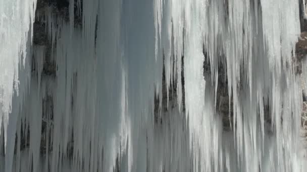 クローズアップ冬の川カスケードは白い輝くつららに凍った 冬の日に岩山の崖からぶら下がる見事な霜のつららが 凍った滝の水滴を溶かす早春の太陽を溶かす — ストック動画