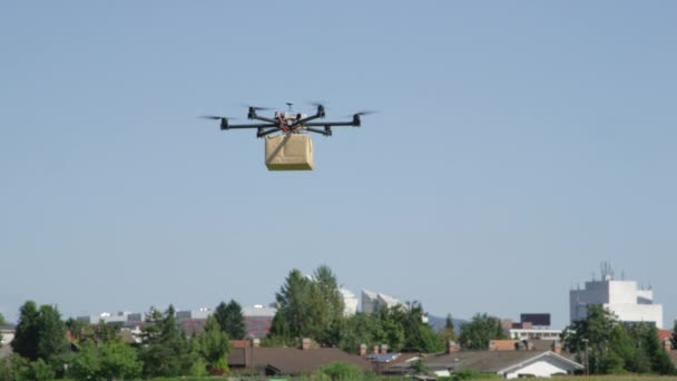 クローズアップ Uavドローン配信 都市に大きな茶色のパッケージを飛ぶマルチコプター あなたの家にポストパッケージを配信ドローン ヘリコプタードローンによる未来的な出荷 マルチコプターロジスティクスと輸送 — ストック動画