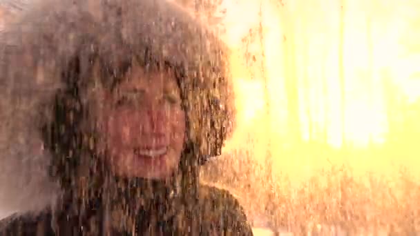 慢动作肖像 闪闪发光的雪花飘落在夕阳下 在温暖的冬衣上快乐微笑的年轻女子 在夕阳森林里 在欢快的女孩头上下雪 冬天的人 — 图库视频影像