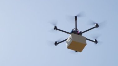 Yakın Uav insansız hava aracı teslimatı. Multicopter mavi gökyüzü üzerinde büyük kahverengi paket uçan. Drone evinize posta paketi teslim. Helikopter drone ile fütüristik sevkiyat. Multirotor lojistik ve taşımacılık