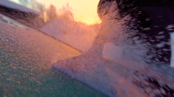 スローモーションクローズアップDof 人は黄金の日の出に車の窓から朝の霜を掃除します 凍った車のフロントガラスから手を削り取り 太陽の上を流れる雪片 霜を取り除くスクレーパー — ストック動画
