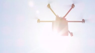 Yakın Çekim Lens Flare: İhA drone teslimat. Multicopter uçan kahverengi paket güneş üzerinde. Drone evinize mal teslim ediyor. Helikopter drone ile fütüristik sevkiyat. Multirotor lojistik ve taşımacılık
