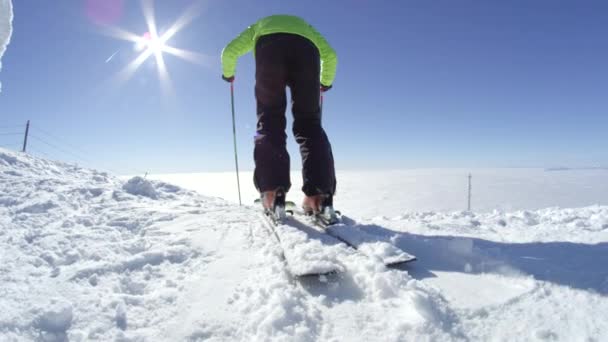 スローモーションワイド 若いアクティブなスキーヤーは 山の頂上で晴れた完璧な寒い冬の日にスタートから離陸します 後ろに太陽フレアでカメラに雪を吹きかける グリーンジャケット着用 — ストック動画