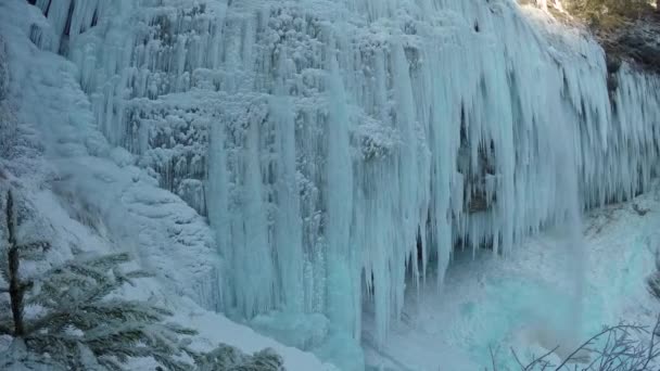 冬の日に岩山の崖の見事な凍った滝のつららをクローズアップ 冬のカスケードは 多数の白いつららに凍結しました 何百本ものつららを越えて滝が落ちる 冬のワンダーランド — ストック動画