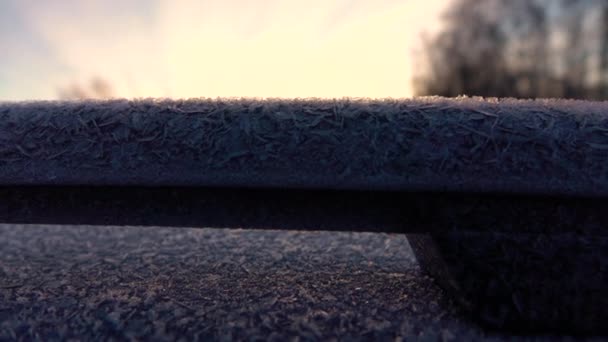 スローモーションクローズアップDof 黄金の日の出に凍った車に美しい朝霜 冷凍車の屋根とフロントガラスに輝くホアフロスト 冷たい朝の太陽の下で輝く冷たい車の氷の雪 — ストック動画
