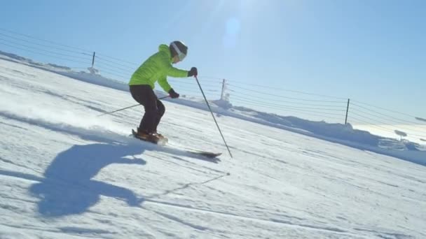 トラッキングスローモーションヤングスキーヤーは 背景にスキーリフトと新鮮な手入れピストで趣味のスキーのための冬の日に牧歌的な完璧な天気を楽しんでいます アルプスに位置するスキーリゾート ヨーロッパ — ストック動画