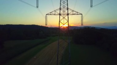 Havadan: Güzel kırsal kırsal alanda tarım alanında saman balyaları üzerinde tepelerin arkasında altın güneşe doğru uçmak. Muhteşem gün doğumunda pastoral tarım arazilerinde elektrik direkleri ve elektrik hatları