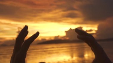 Slow Motion Close Up Siluet: Kız plajda tropikal bir akşam elleri ile romantik bir kalp şekli yapar. Genç kadın okyanus üzerinde parmaklarını bir araya getiriyor ve gün batımında bir kalp yapar