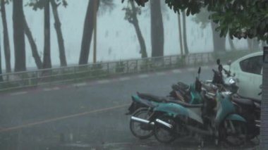Yavaş Hareket: Cezalandırıcı bir muson mevsimi sırasında park halindeki motosikletlerin üzerine büyük su damlacıkları düşer. Şiddetli tropikal yağış kasvetli Tayland boş yolun kenarında terk motosiklet ve araba yıkar.