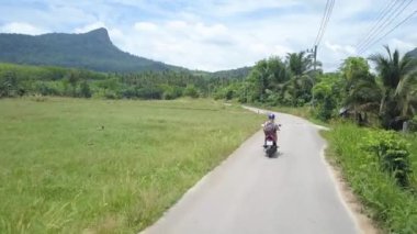 Anten: Bilinmeyen kadın gezgin yemyeşil tropikal doğa ile çevrili güneşli yolda onu kırmızı scooter sürmek. Maceracı genç kadın bir motosiklet kiralar ve nefes kesen yağmur ormanlarına doğru sürmek.