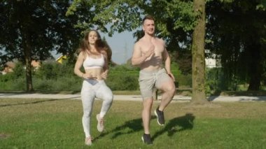 Slow Motion: Güneşli bir yaz gününde parkta koşan mutlu zinde bir çift. Neşeli Kafkasyalı kız arkadaş ve erkek arkadaş doğadaki eğlenceli eğitimleri için ısınıyorlar. Genç adam ve kadın spor yapıyor..