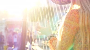 Slow Motion, Close Up, Lens Flare, Copy Space günbatımında arp çalan tanınmayan sarışın kadın. Bilinmeyen kadın sokak sanatçısı bir arp çalıyor ve turistleri eğlendiriyor..