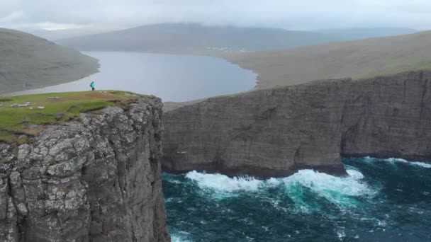 コピースペース 壮大な荒波と絵のような北欧の風景を見下ろす芝生の崖の端に向かって認識できない若い女性のハイキング フェロー諸島の観光トレッキング — ストック動画