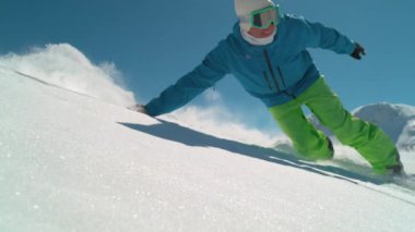 Slow Motion Close Up: Güneşli kış gününde dağlarda snowboard yapan gülümseyen kaykaycı. Kameranın önünden toz kar süren serbest kayakçı taze kar yüzeyinde el sürüyordu. Arka planda kayak