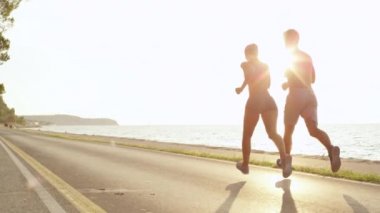 Slow Motion, Copy Space, Sun Flare: Boş asfalt yolda güzel bir okyanus manzarasıyla koşan formda genç antrenman arkadaşları. Tanımlanamayan çift deniz kenarında egzersiz yapıyor..