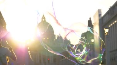 Slow Motion, Close Up, Lens Flare, Dof: Erkek sokak sanatçısı Roma 'daki tarihi katedralin yakınında büyük sabun köpükleri yapıyor. Gün batımında renkli kabarcıklar yaparak turistleri eğlendiren sokak sanatçısı.