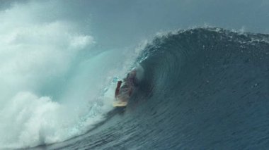 Slow Motion, Close Up: Profesyonel sörfçü parlak güneş ışığında parıldayan güzel bir tüp dalgasında sörf yaparken elini suyun içinde sürüklüyor. Genç sörfçü neredeyse büyük bir fıçı dalgası tarafından süpürülecek..