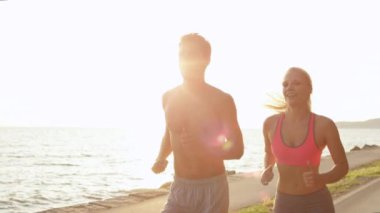 Slow Motion, Sun Flare, Close Up: Gülümseyen atletik sevgili ve kız arkadaş Slovenya 'da güzel bir sahil patikası boyunca koşuyorlar. Neşeli antrenman arkadaşları deniz kenarında koşuştururken eğleniyor.