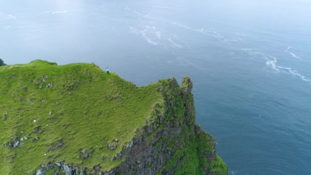 航空写真 芝生の崖の端から写真を撮るカメラマンの息をのむショット 美しい青い海を撮影するフェロー諸島の旅行をハイキングに認識できない若い女性を停止します — ストック動画