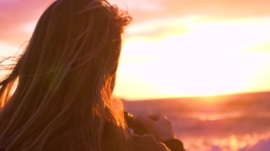 Slow Motion, Lens Flare, Copy Space, Close Up: Genç bayan fotoğrafçı güzel akşam güneşine ve sahile doğru sıçrayan küçük deniz dalgalarına bakıyor. Bir kız ve gün batımının sinematik görüntüsü.
