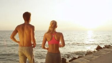 Slow Motion, Close Up: Atletik genç adam ve kadın okyanusa koşup kollarını başlarının üstüne kaldırdılar. Yaz tatilinde sporcu eşleri deniz kenarında eğlenceli bir antrenmanı bitirmeyi kutlarlar..