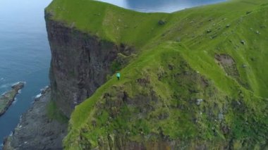 Hava, Zaman Bükülmesi: Manzaralı bir yolculukta olan bir kadın, yüksek otlak bir uçurumun kenarından fotoğraf çekiyor. Kallur Deniz feneri yakınlarında yürüyüş yapan kadın fotoğrafçının muhteşem uçuş manzarası..