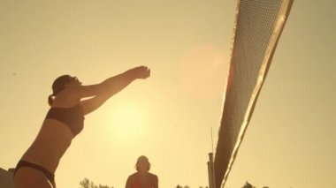 Yavaş Hareket, Düşük Açı, Yakın Çekim, Lens Parlama: Genç kadın voleybolcular pas ve güneşli bir yaz akşamı net üzerinden topu başak. Fit Kafkas kızlar gün batımında plaj voleybolu oynuyor.