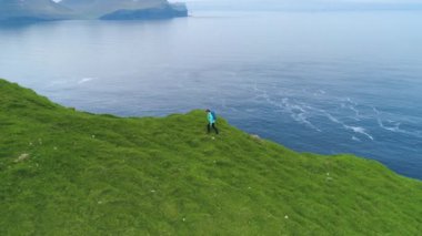 Hava: güzel okyanus ve doğal yeşil Faroe Adaları mükemmel bir resim elde etmek için bir dik çimenli tepeye hiking genç kadın fotoğrafçı uçan. Kadın sakin dağlarda maceraya.