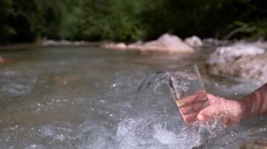 Slow Motion, Close Up: Tanınmayan kız ferahlatıcı kaynak suyunu büyük şeffaf bir bardağa dolduruyor. Genç bir kadın elinde bir bardak tutuyor ve bir orman deresinden soğuk suyu topluyor..