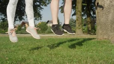 Slow Motion, Low Angle Close Up: Bilinmeyen erkek arkadaş ve kız arkadaş güneşli havalarda zıplıyor. Tanımlanamayan atletik erkek ve kadın antrenman partnerleri açık hava egzersizleri için ısınıyorlar..