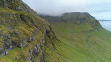Boş çayırlara bakan kayalık dağlara yakın uçmak ve sisli bir günde Faroe Adaları 'nda sakin bir deniz. Engebeli kıyı manzarası ve İskandinavya 'daki sarp otlak tepeler..